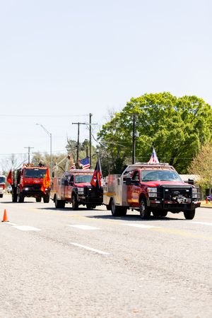 Red fire trucks decorated with American flags parade down a sunny small-town street during a patriotic community celebration.