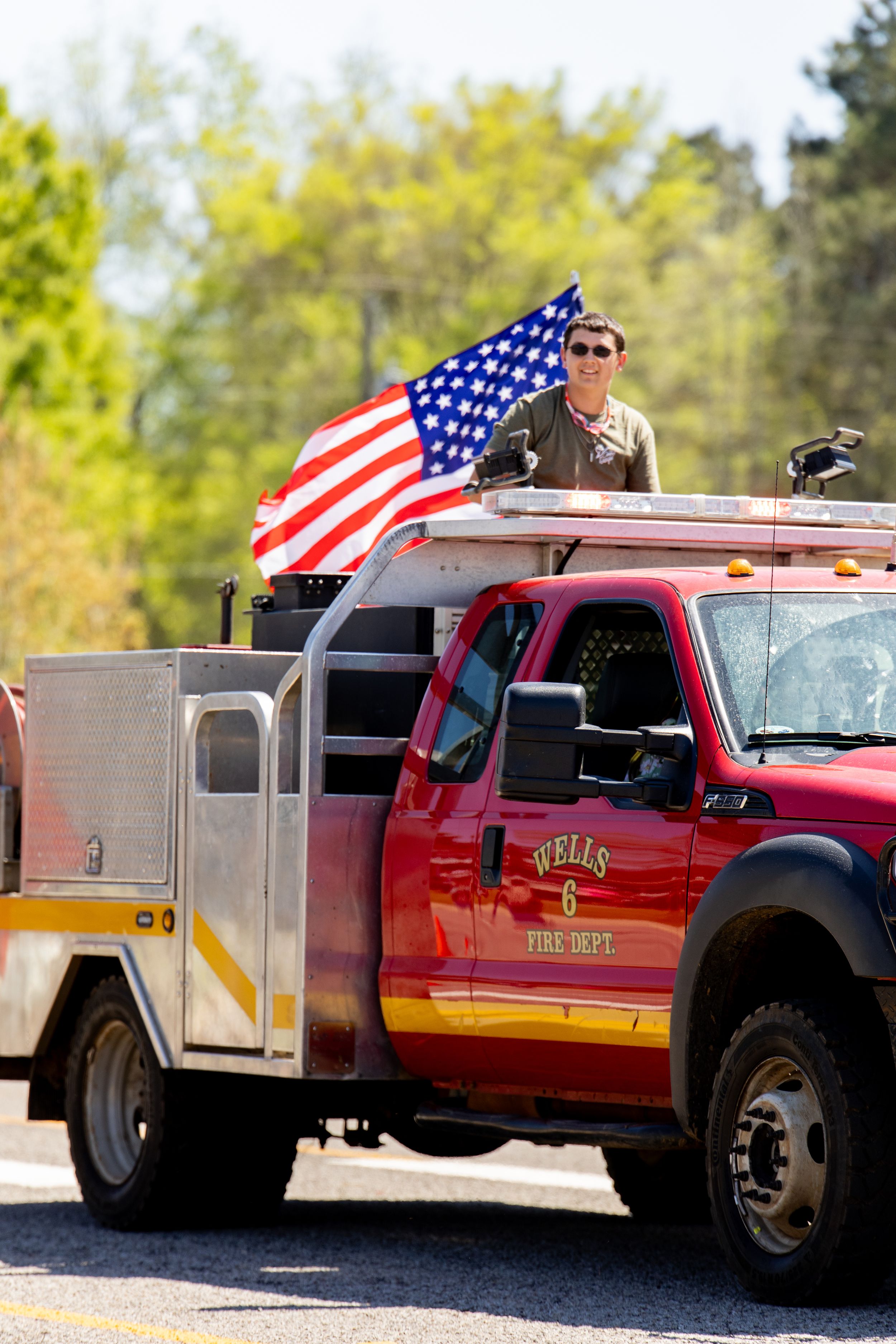 Person holding American flag on Wells Fire Dept. red truck during parade.