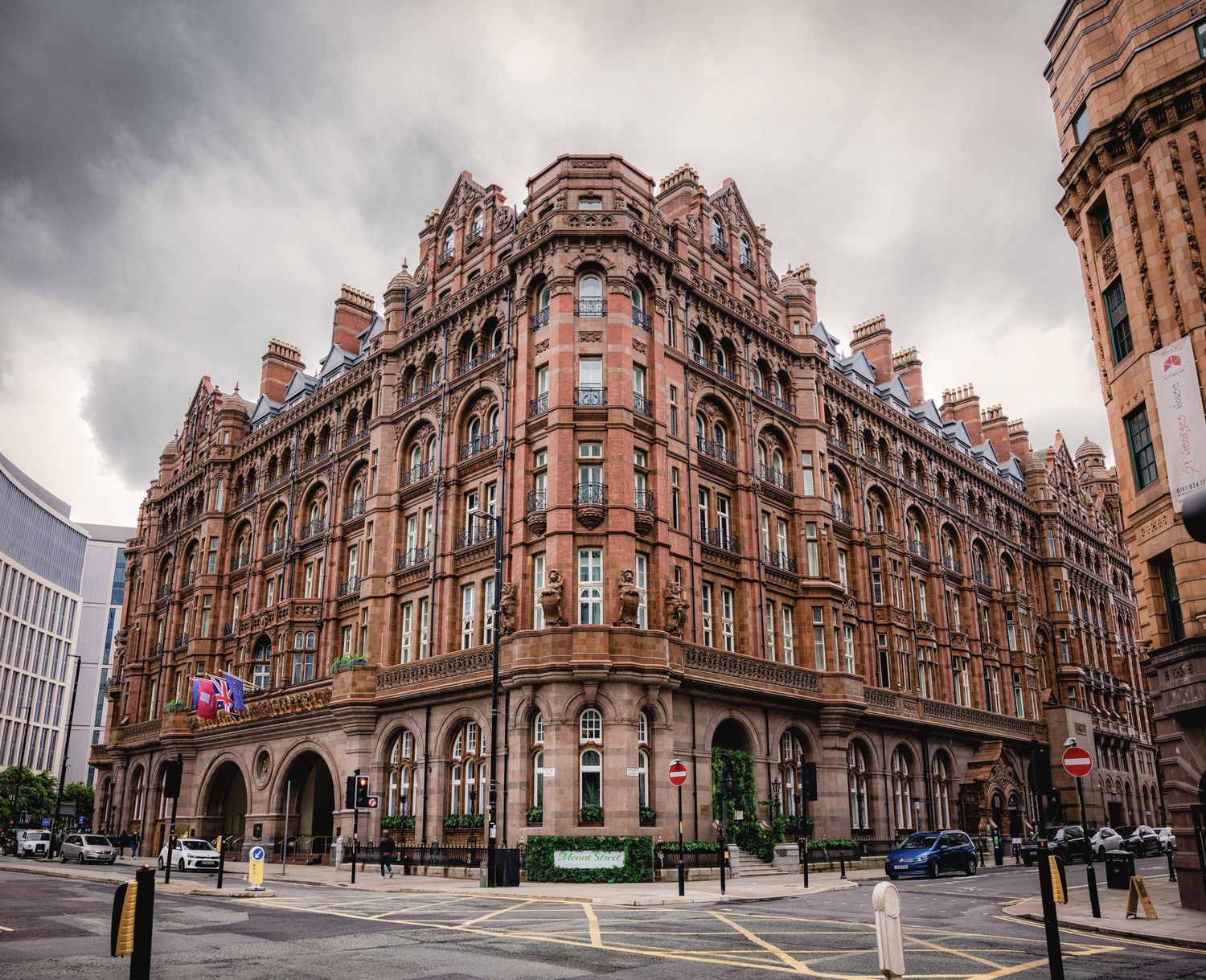 Grand Victorian red-brick corner building with ornate Gothic architecture under dramatic cloudy skies in Manchester.