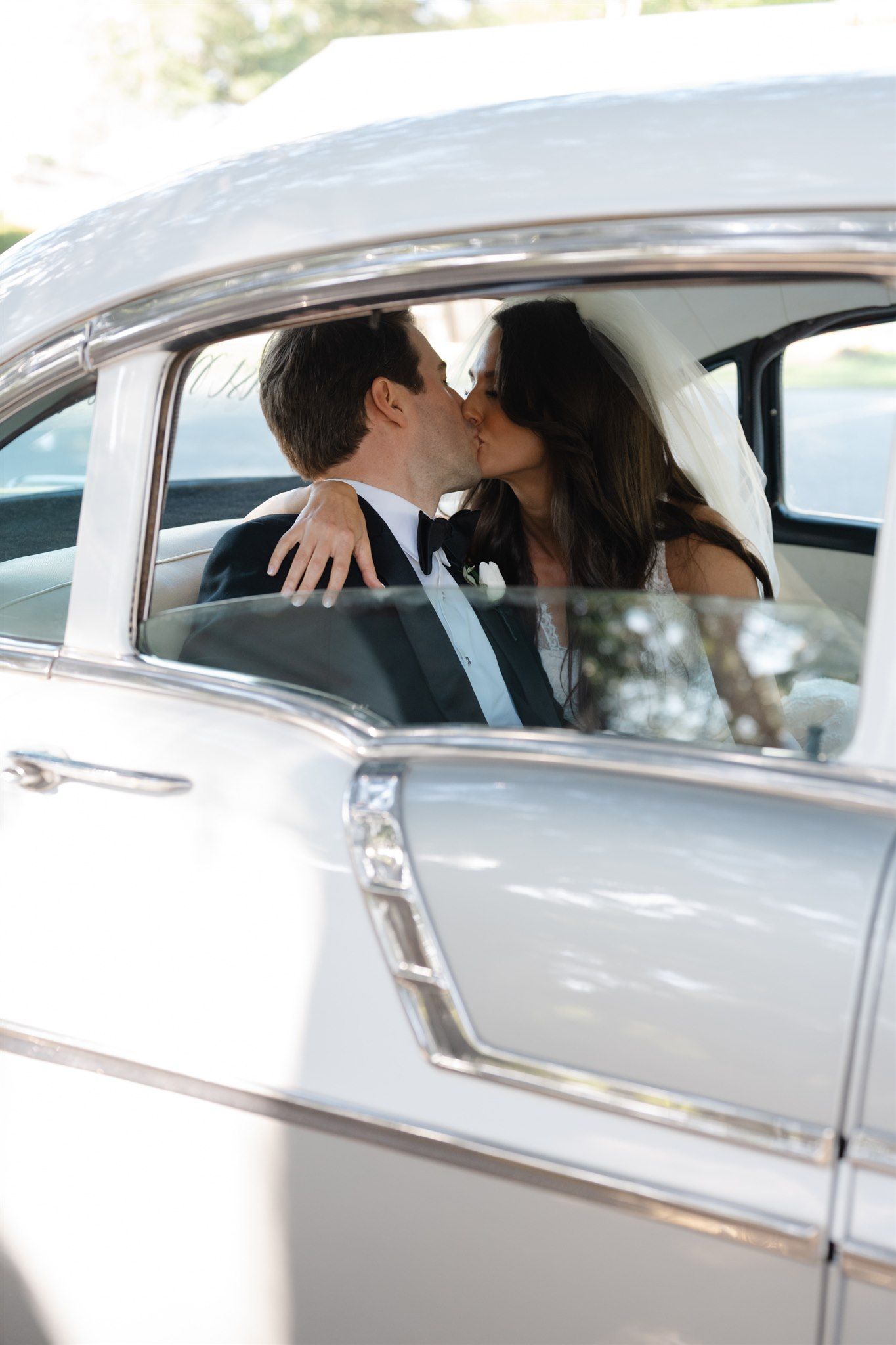 Happy newlyweds waving from vintage classic car window in black and white wedding photo.