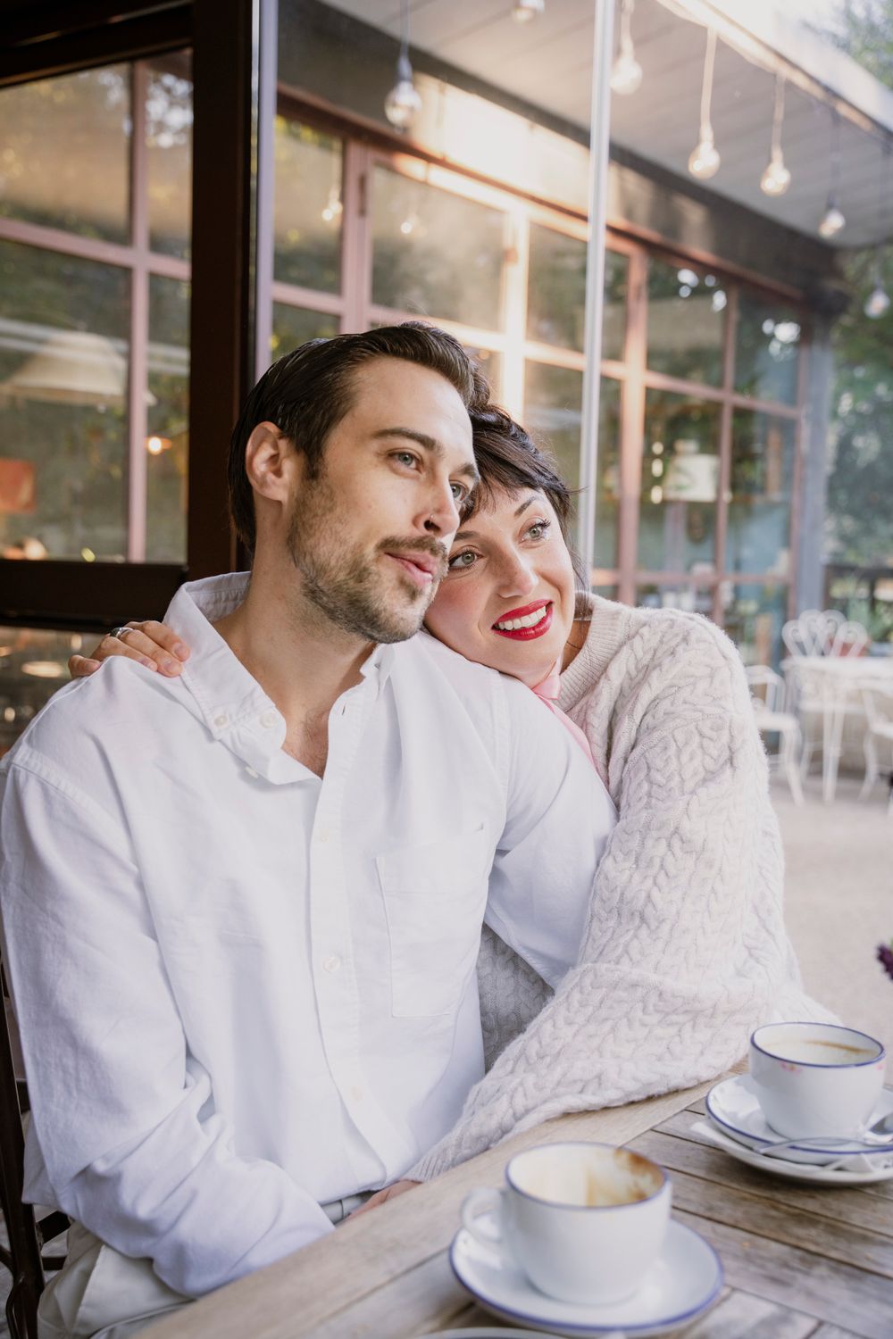 Romantic couple sharing a coffee at an outdoor cafe, woman smiling with red lips.