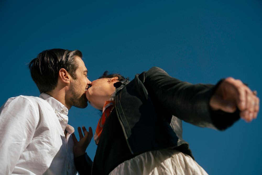 Couple sharing a passionate kiss against a vivid blue sky outdoors.
