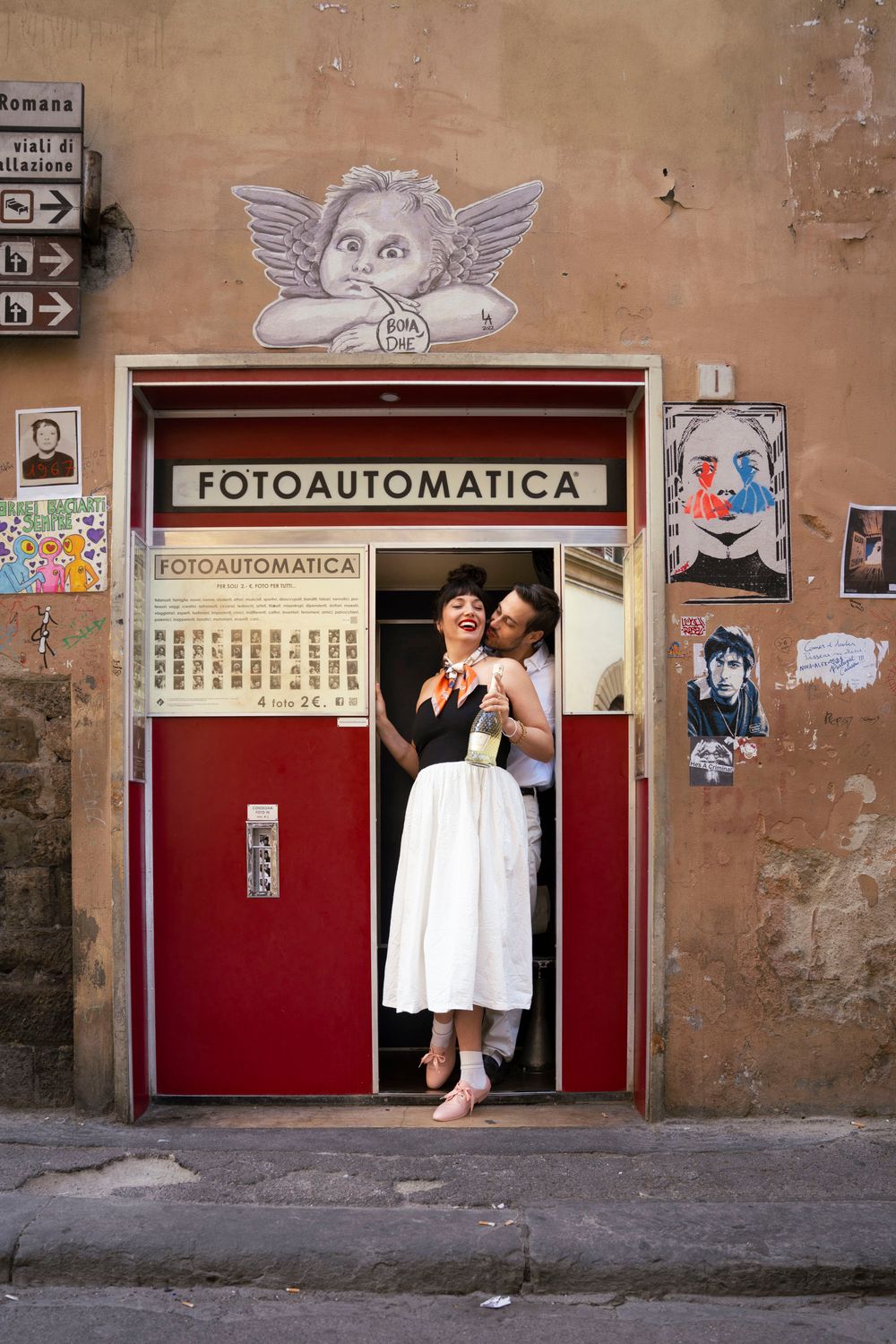 Joyful couple posing in a Fotoautomatica photo booth doorway on an Italian street.