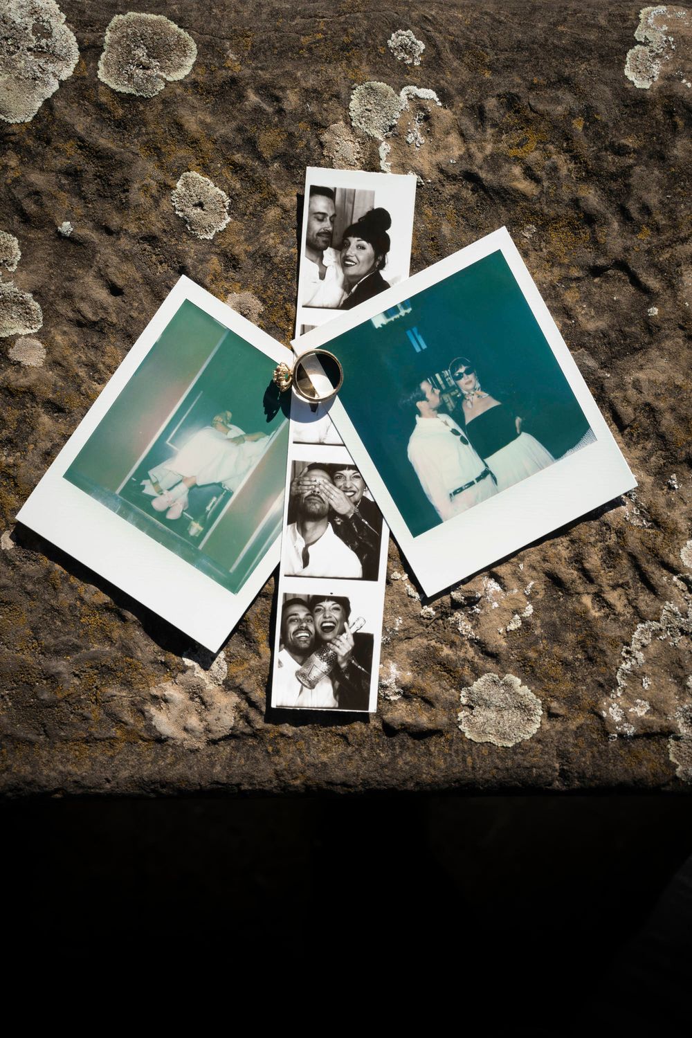 Polaroid photos and wedding rings arranged on a textured stone surface.