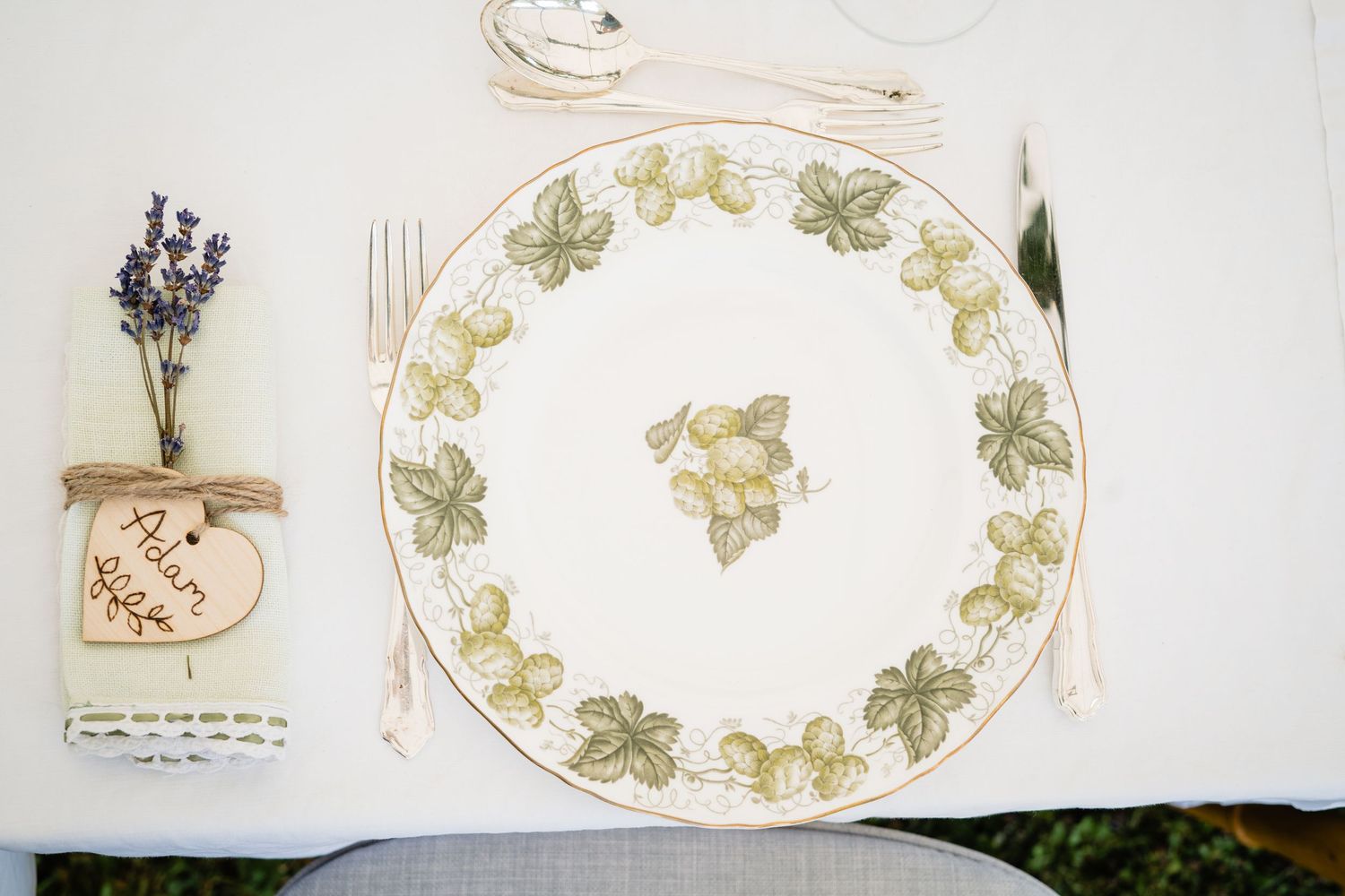 Elegant place setting with floral vine plate, lavender bundle, wooden name tag, and silverware on white linen.