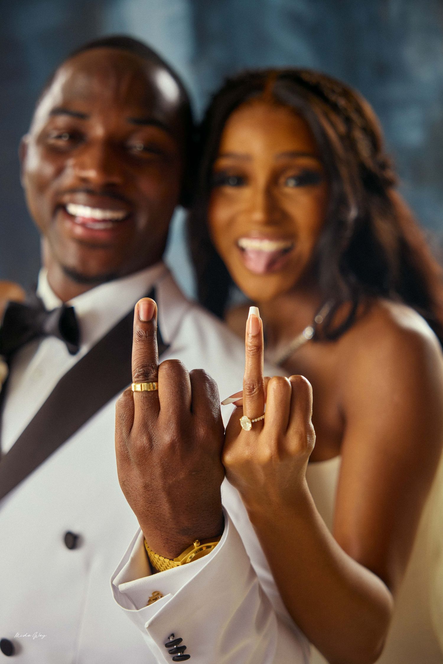 Joyful newlywed couple in wedding attire showing off gold wedding rings on their fingers while smiling and celebrating.