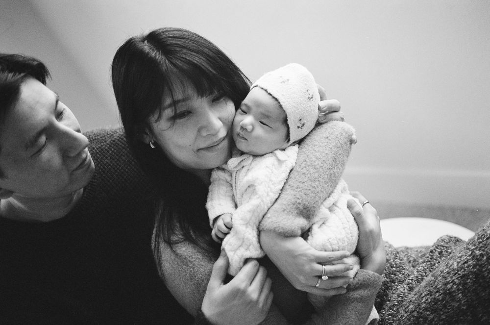 Black and white photo of parents lovingly holding their newborn baby, capturing a tender family moment.