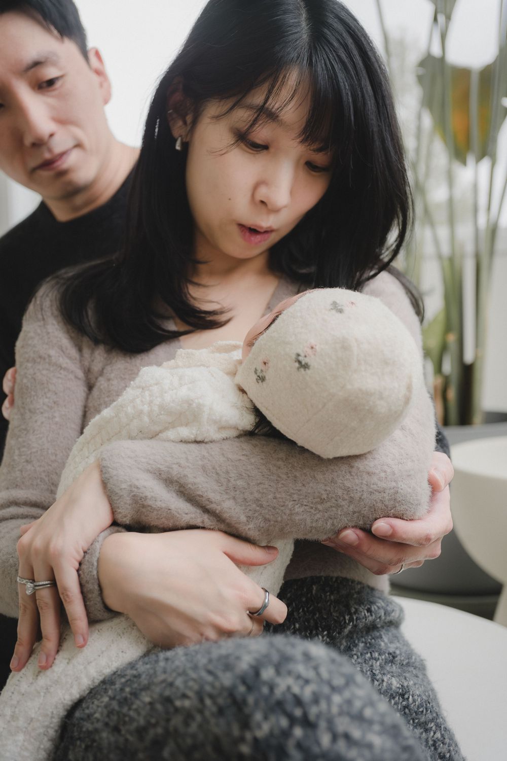 Asian couple sitting together, woman cradling a soft plush stuffed animal toy indoors.