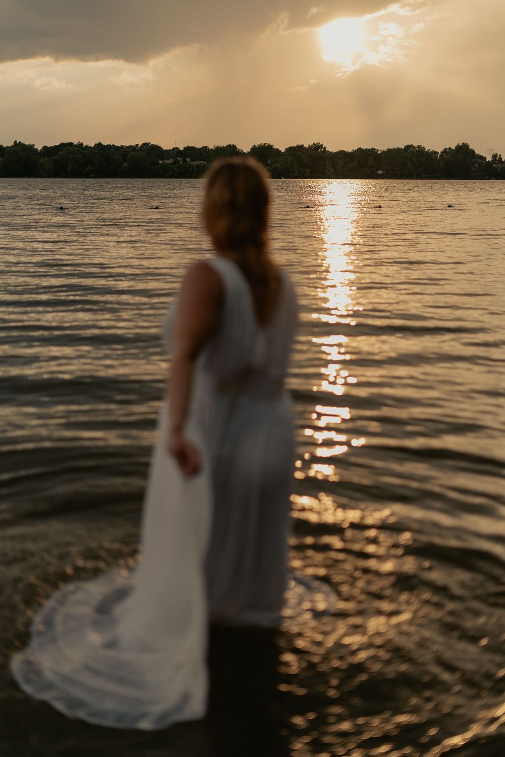 Silhouettes of a couple stand by a lake at sunset with golden light reflecting on rippling water.