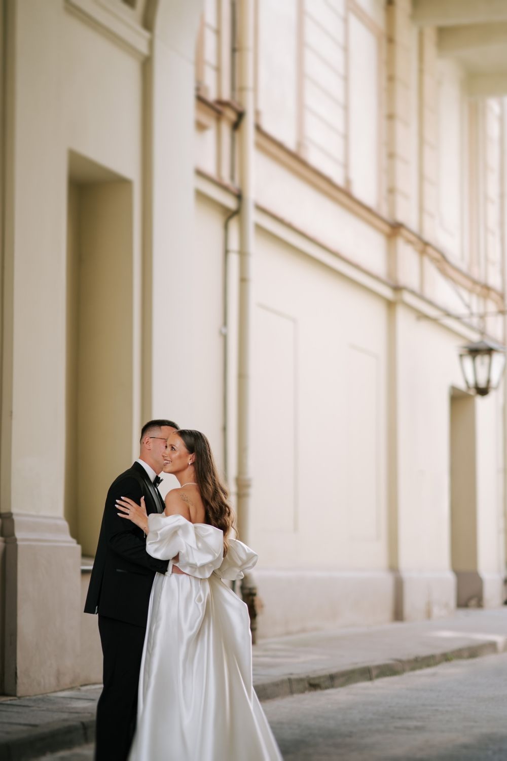 Elegant couple shares intimate moment against white building wall.