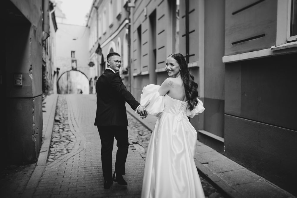 A wedding couple walks through a charming cobblestone alley in black and white photography.
