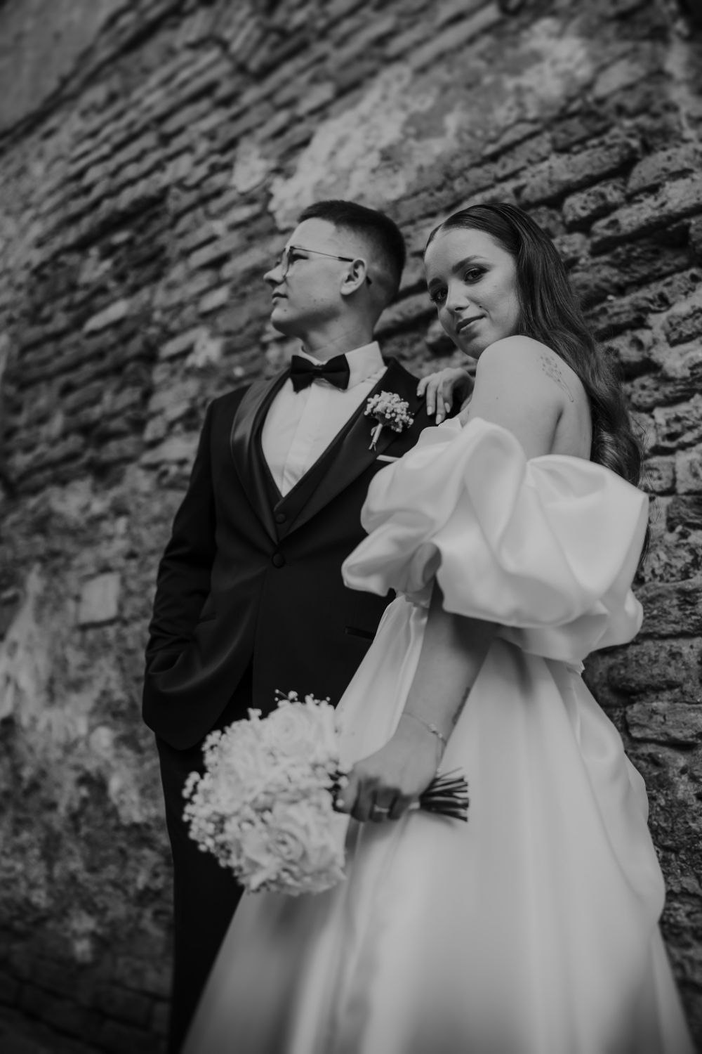 Artistic black and white wedding portraits against a textured stone wall background.