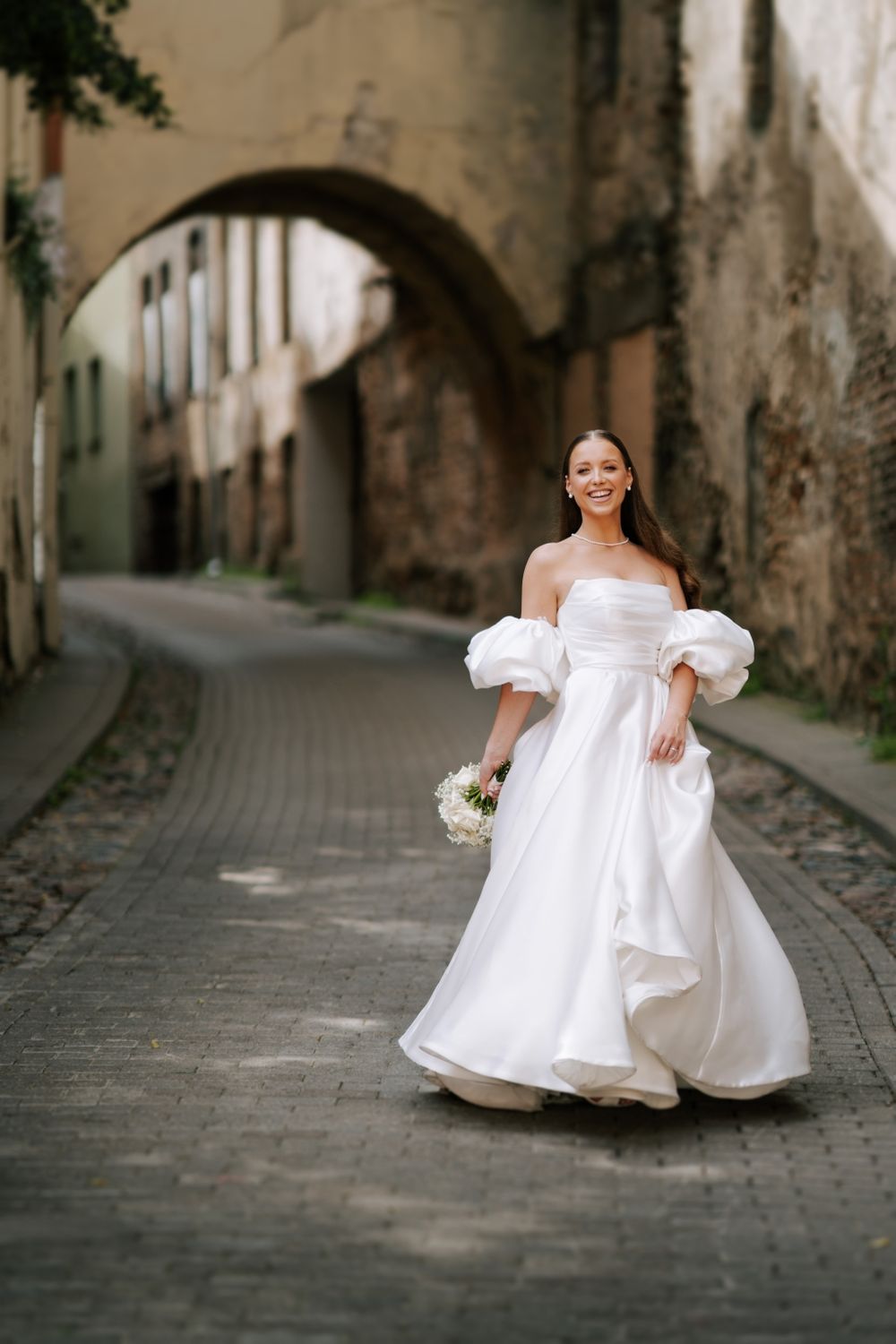 A bride in a flowing white dress twirls on a historic cobblestone street.