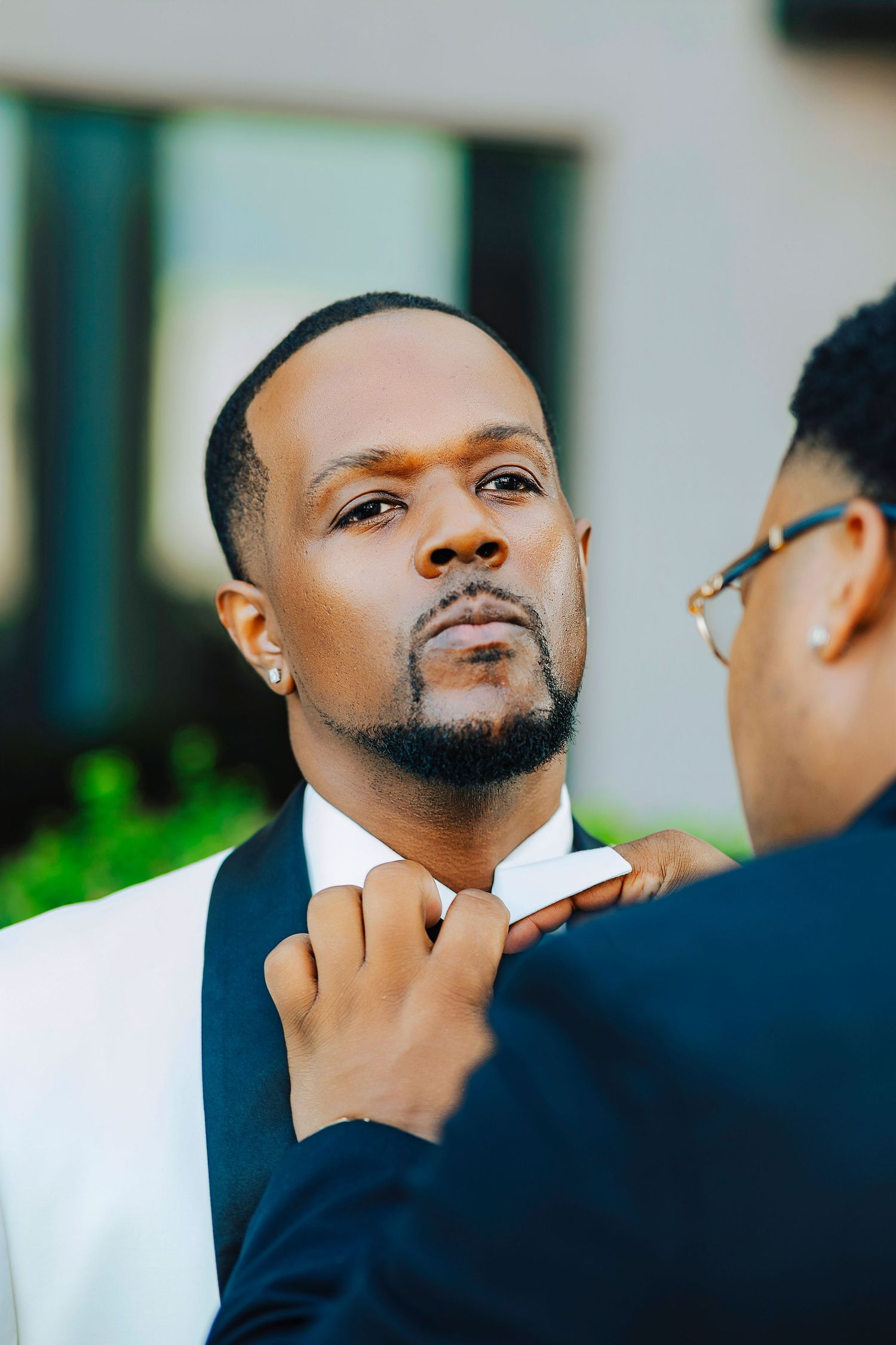 Person in navy suit jacket touching their chin thoughtfully while looking upward in an outdoor setting.