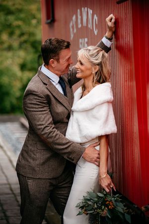 A romantic wedding couple embraces against a red barn wall in a series of intimate poses.