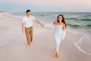 A couple runs joyfully along a pristine white sand beach at sunset with turquoise waves rolling in.