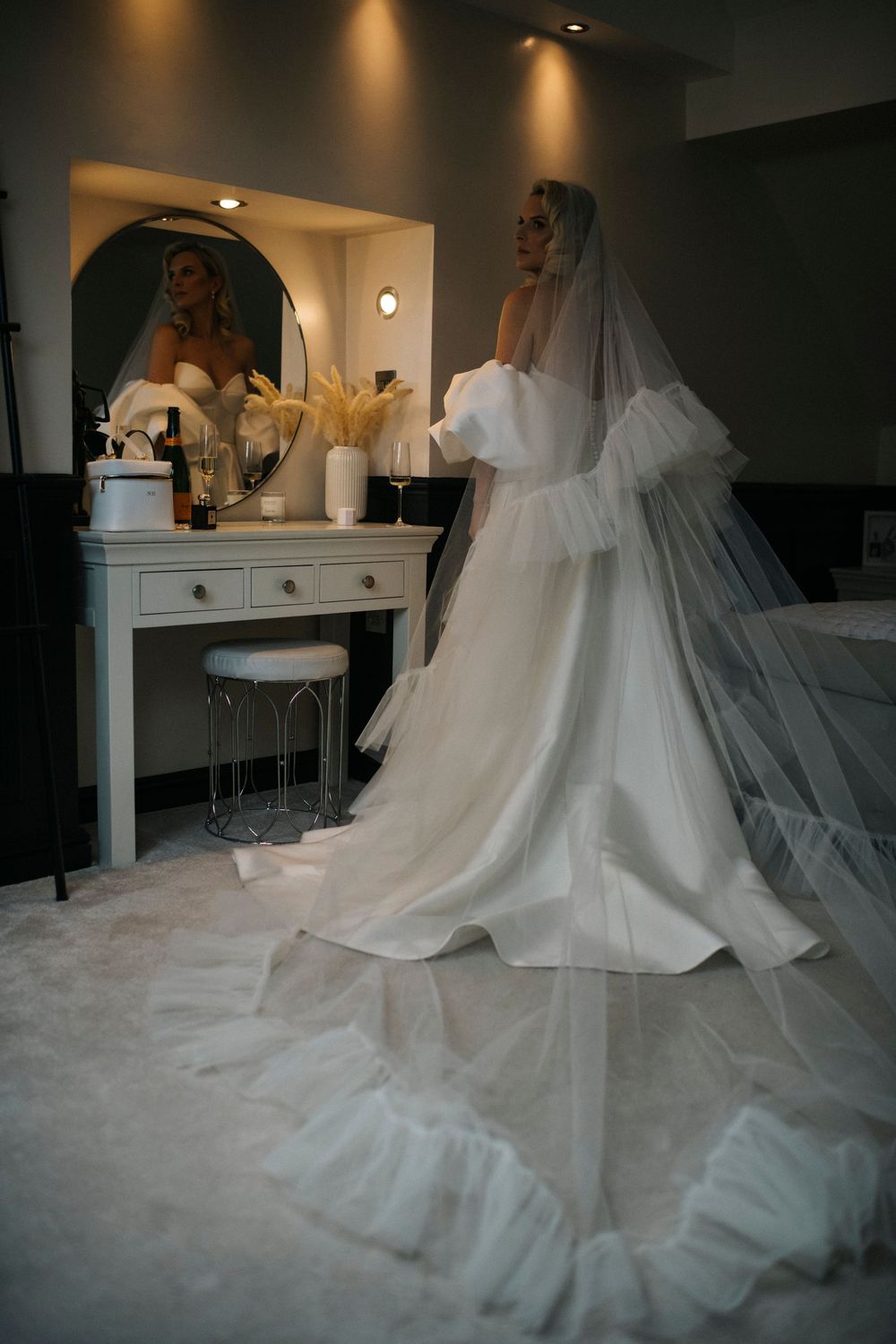 Elegant bridal gown with dramatic train reflected in vanity mirror during wedding preparations.