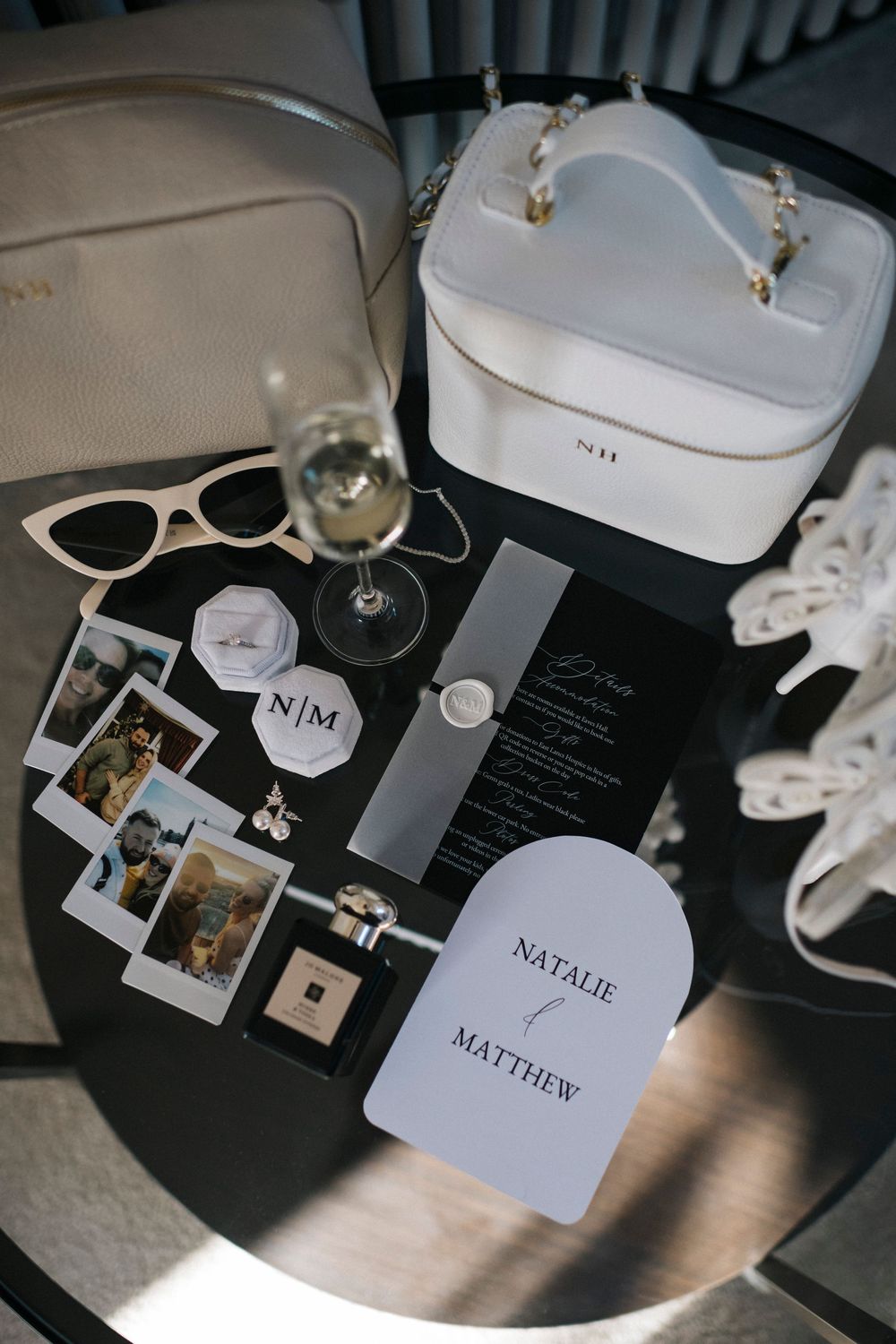 Wedding details including white cosmetic cases, sunglasses, polaroid photos and name cards arranged on a dark surface.