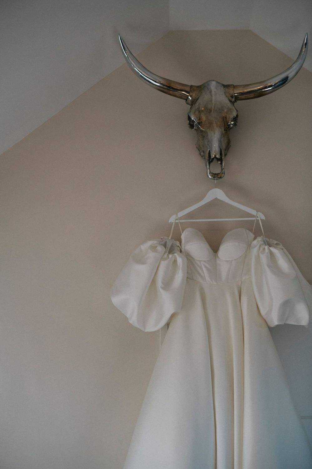 A white wedding dress with puff sleeves hangs elegantly against a neutral wall.