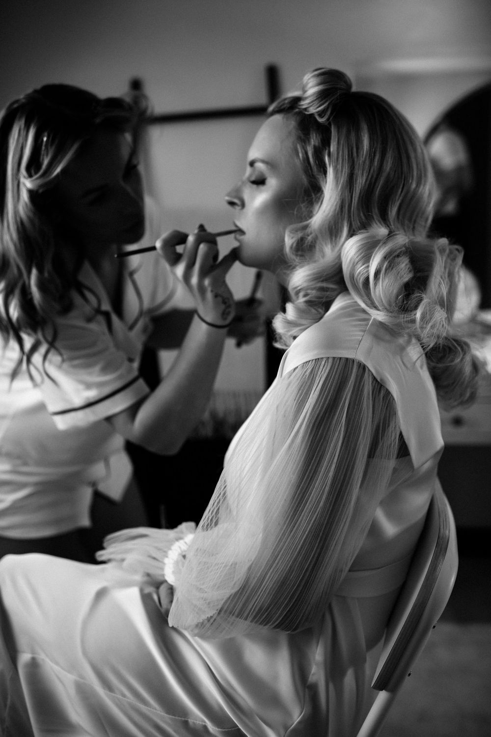Black and white image showing wedding preparations with stylists working on hair and makeup.
