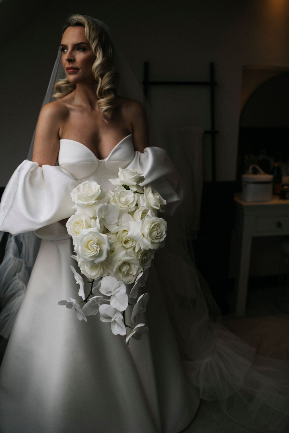 White roses and orchids in a bridal bouquet against a classic wedding dress.