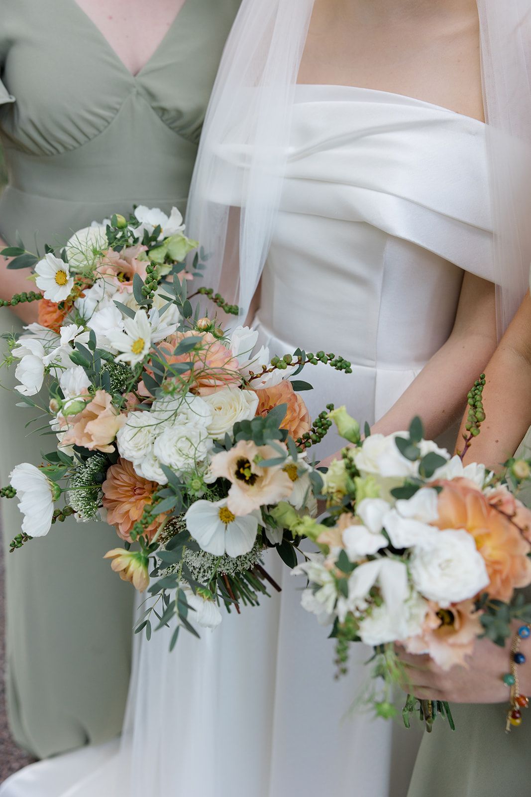 A row of elegant white and peach floral bouquets held against sage green bridesmaid dresses at a wedding.