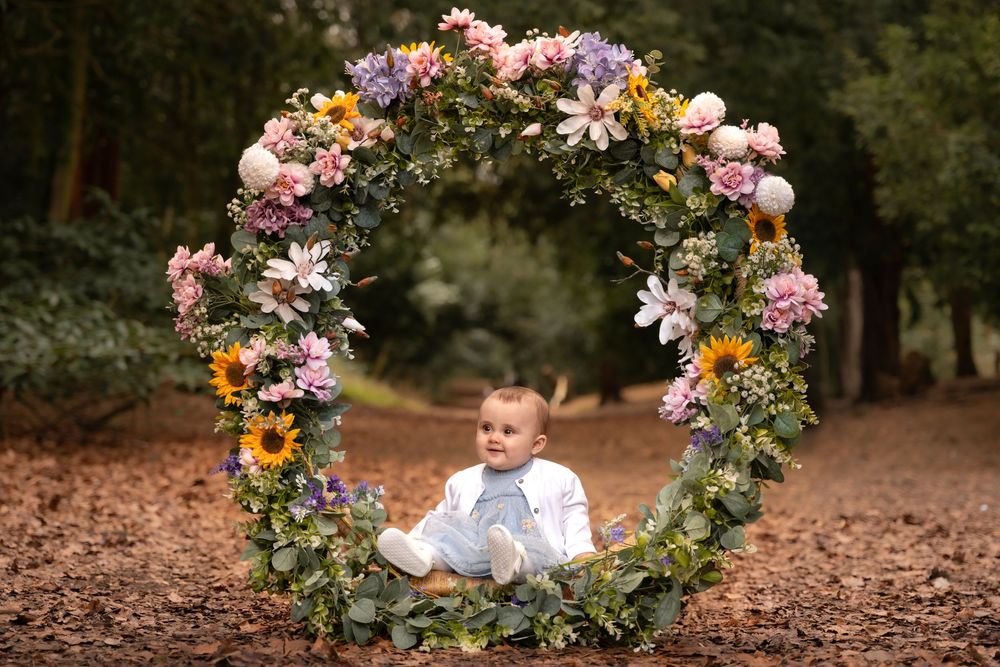 Beautiful floral wreath arch with greenery and pastel flowers sits on rustic forest ground surrounded by autumn leaves.