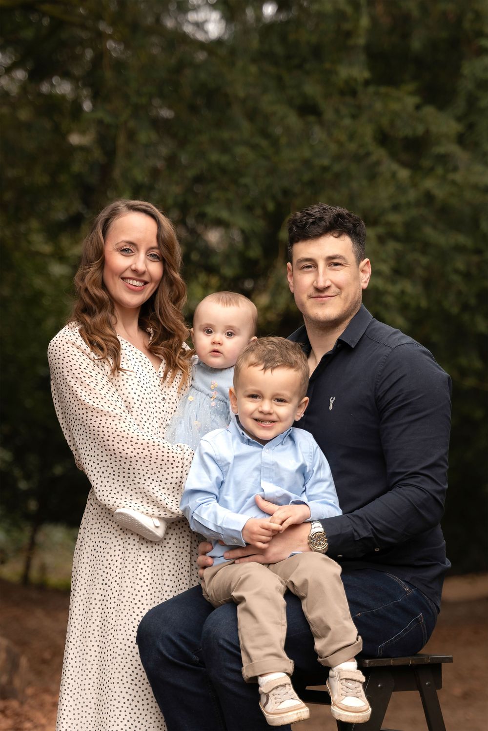 A family poses together outdoors in a wooded setting during an autumn photo session.