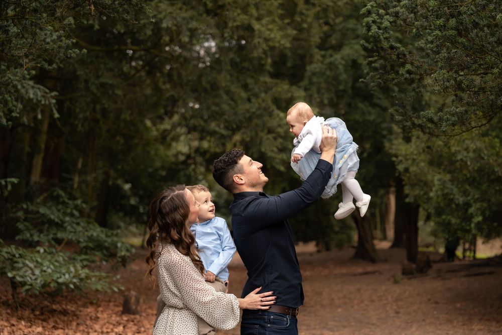 A couple lifts and plays with their baby in a wooded outdoor setting during a family photo session.