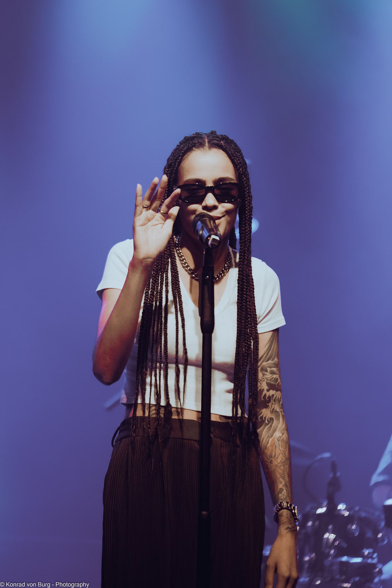 Concert performer with dreadlocks in white shirt against purple stage lighting.