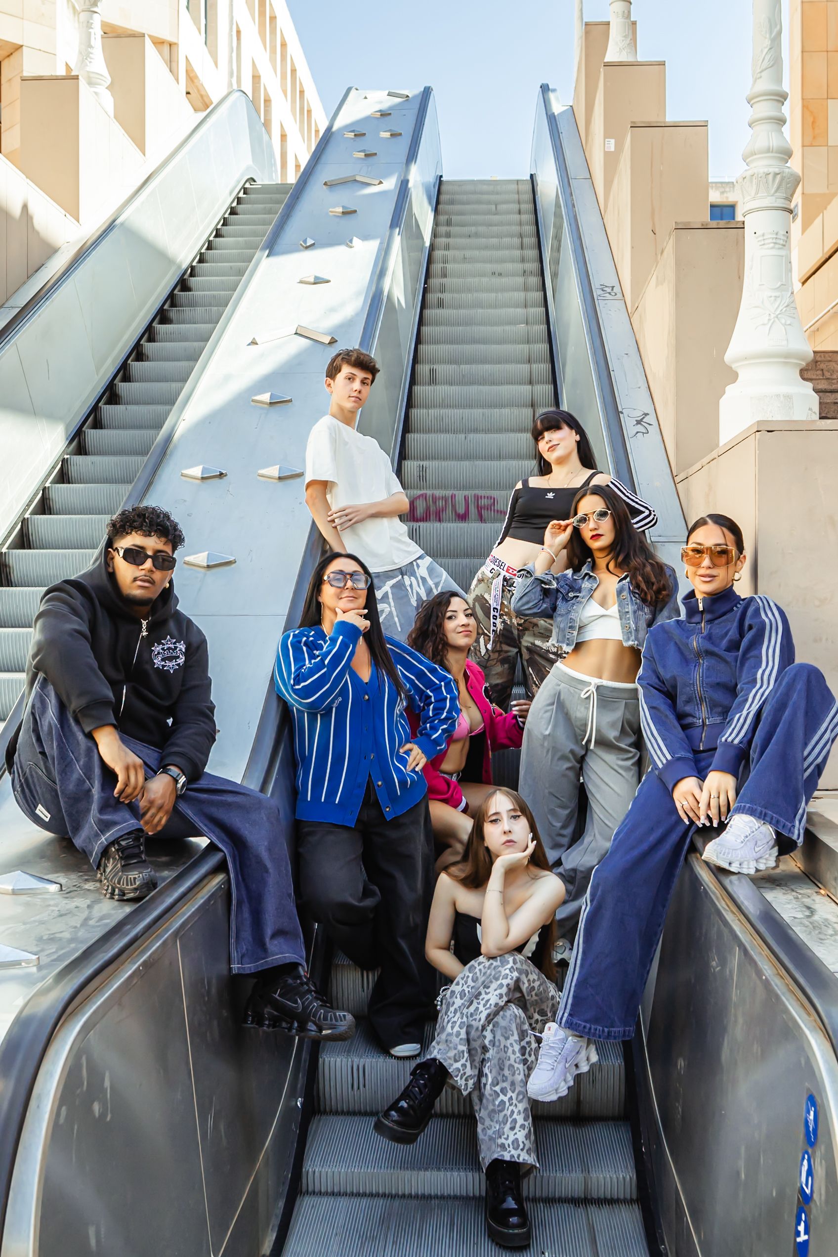 Group of people posing casually on escalator steps in coordinated blue outfits.