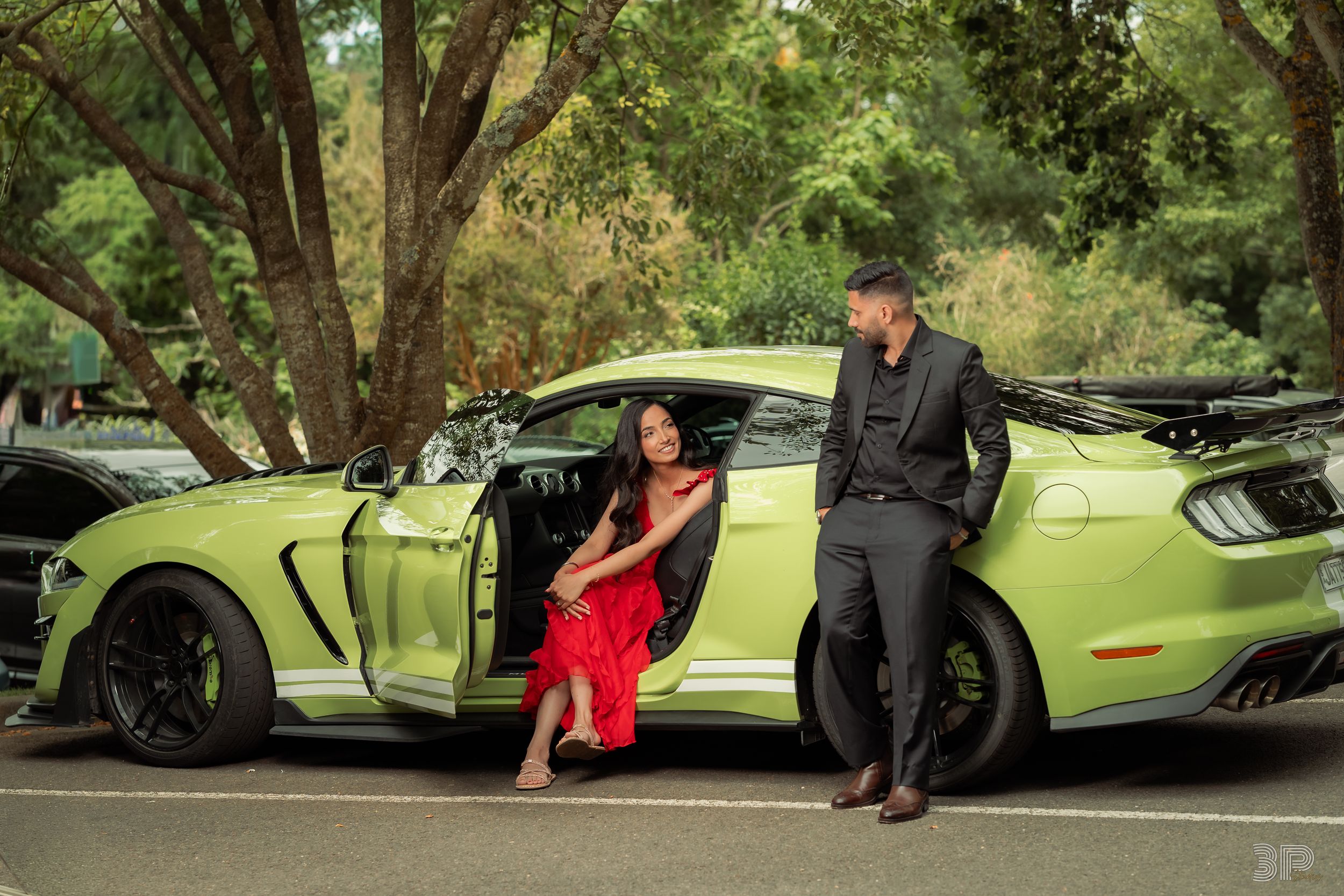 A lime green Ford Mustang GT500 parked under trees with two people posing by the open door.