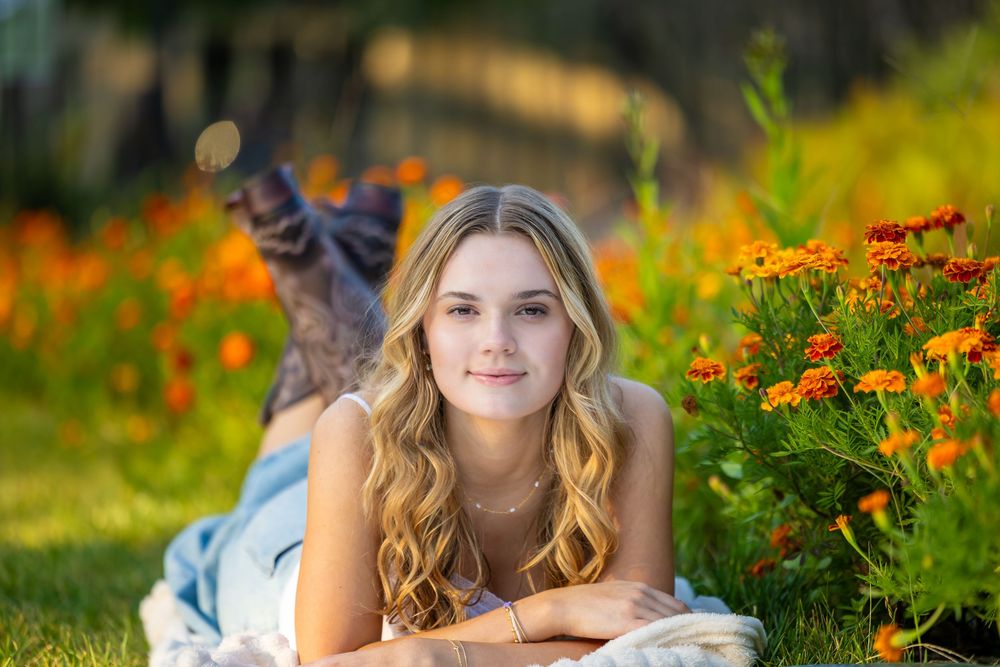 A woman lying in a vibrant garden of orange and yellow flowers during a sunny summer day.