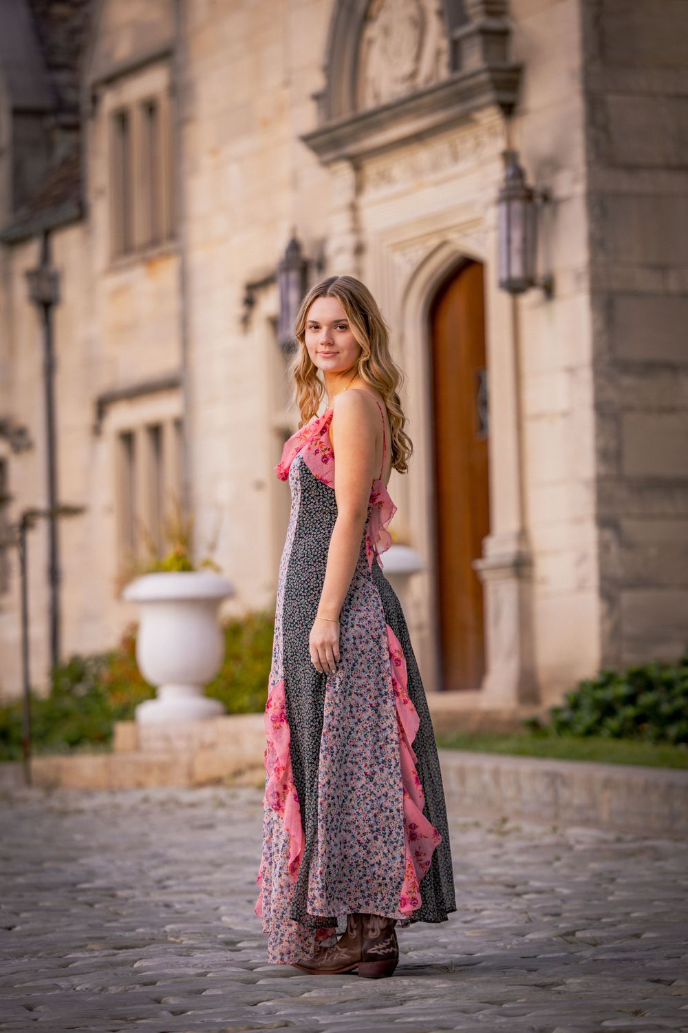 Young girl in a gray dress with pink bow stands on cobblestone street near historic stone building.