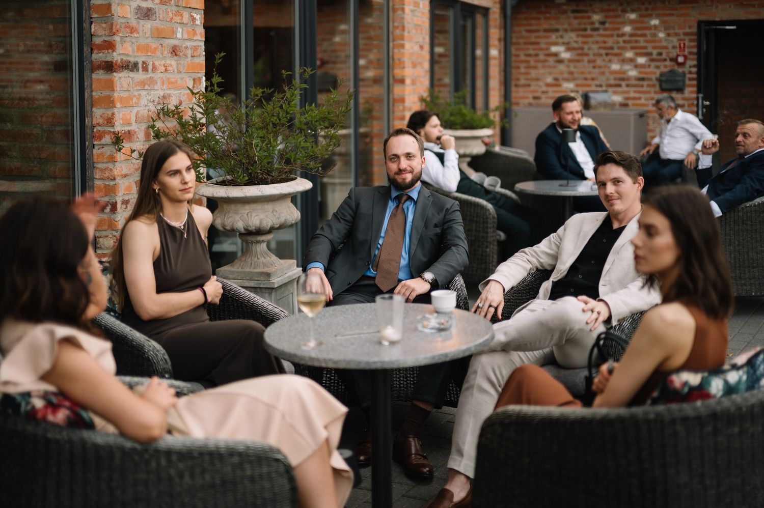 Wedding guests socializing on outdoor patio with brick walls and garden urns.