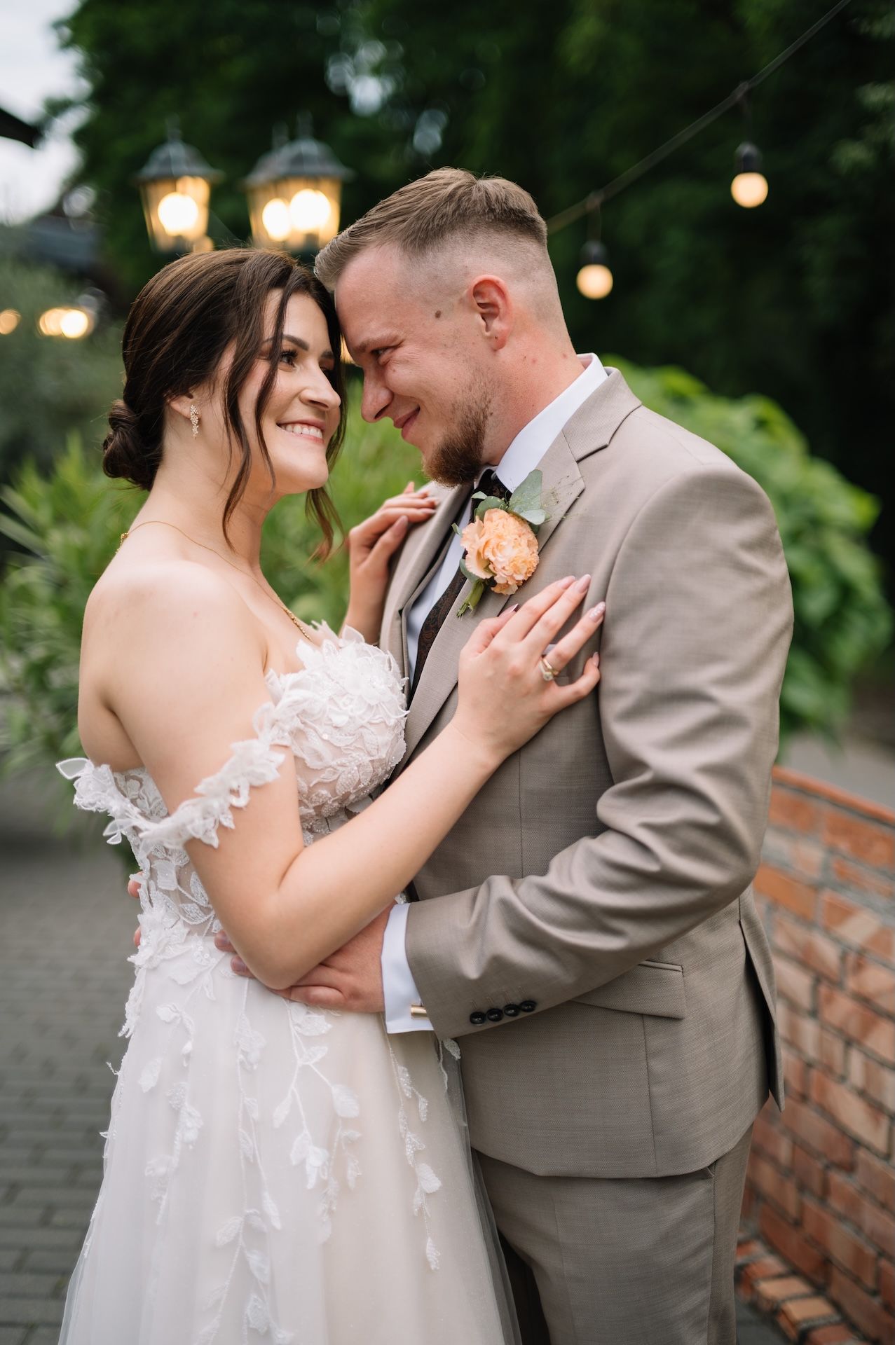 Bride and groom sharing romantic moment outdoors under string lights at dusk.
