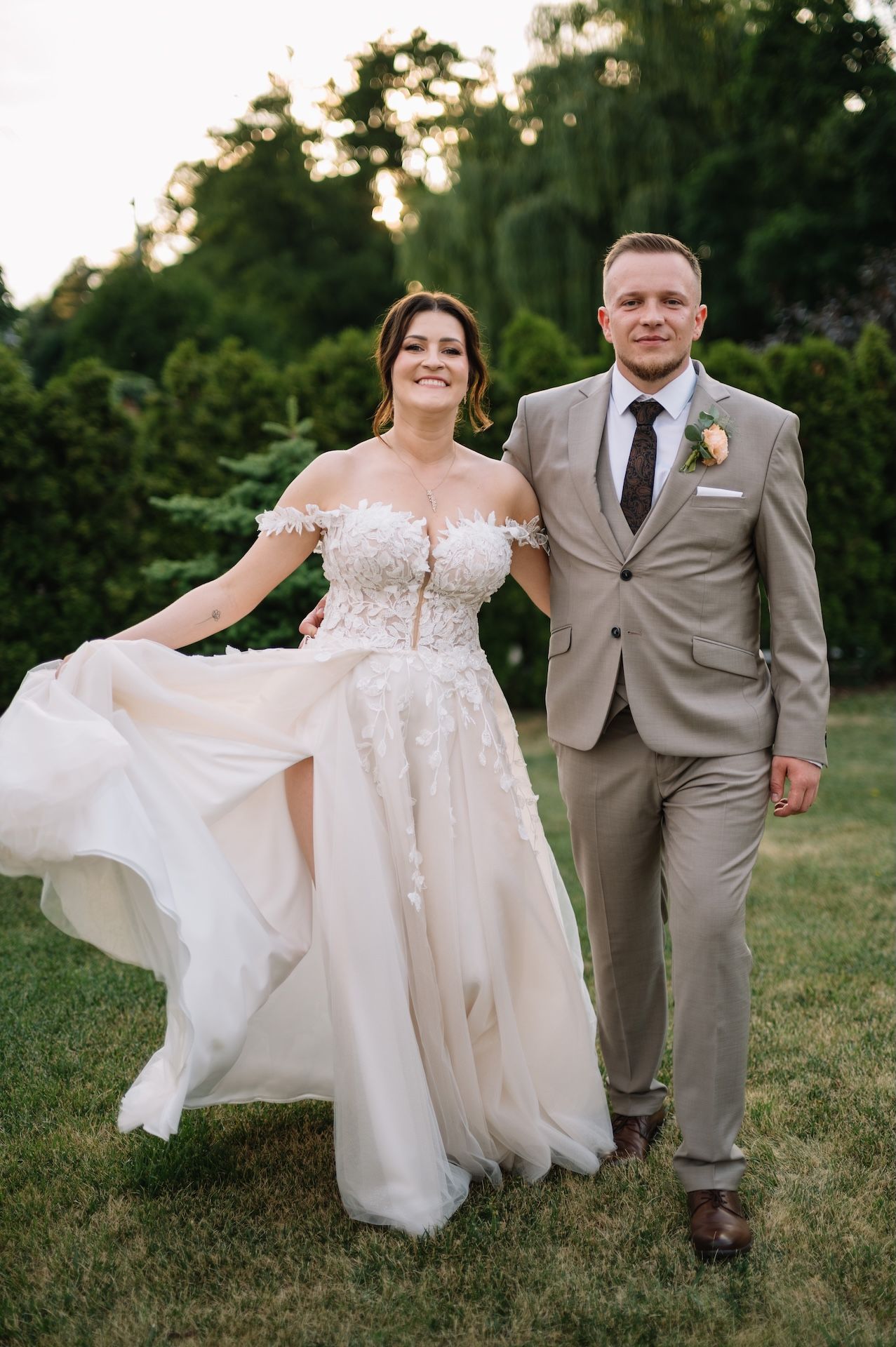 Bride twirls her flowing tulle gown beside smiling groom in tan suit during golden hour garden wedding.