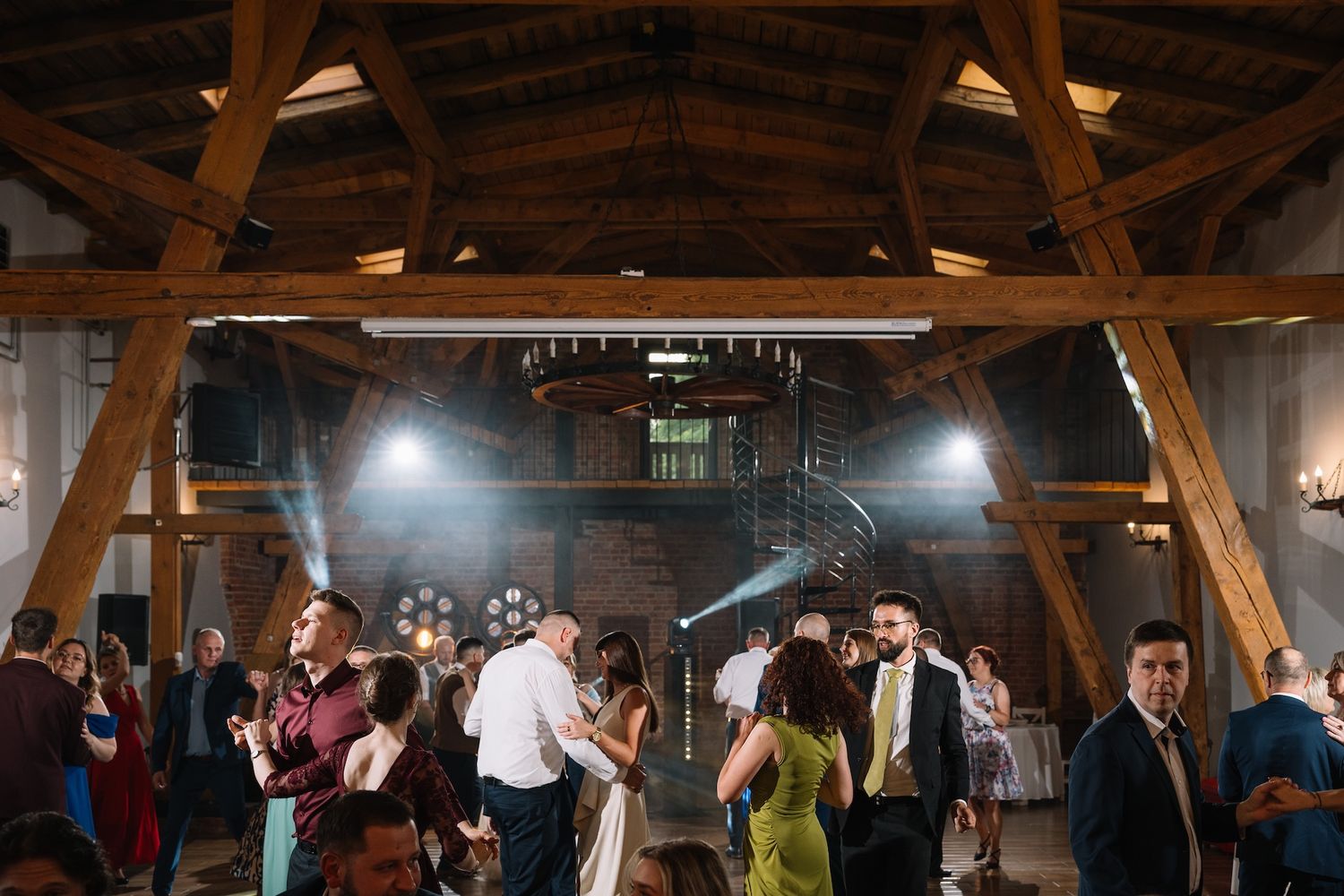 Wedding guests dancing energetically in a rustic barn venue with wooden beams and atmospheric lighting.