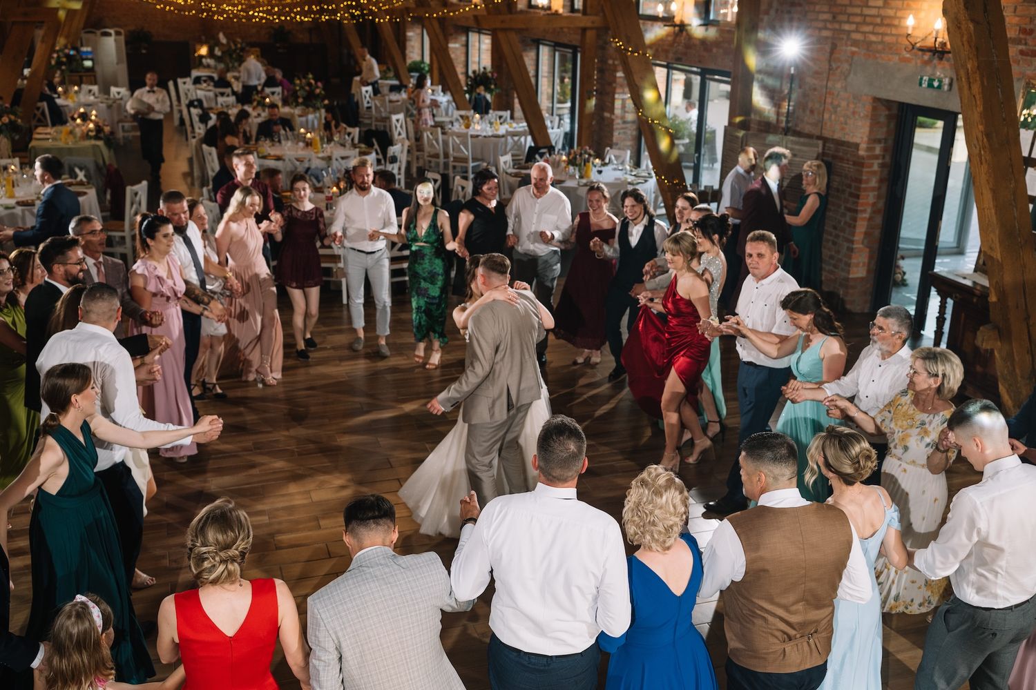 Large group of wedding guests dancing together on the dance floor of a rustic barn reception venue.