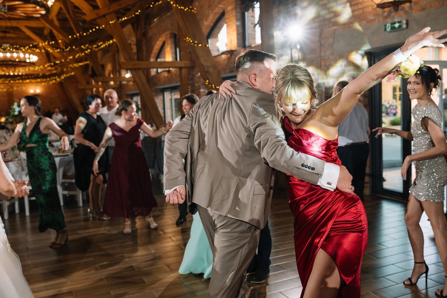 Couple dancing closely at a wedding reception, woman in red dress dips gracefully in a warmly lit barn.