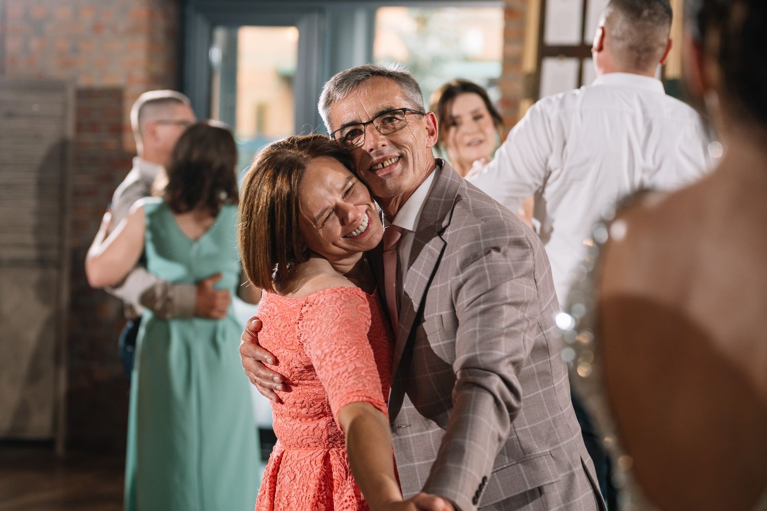 Smiling couple sharing a warm embrace while dancing at a wedding reception in a rustic venue.