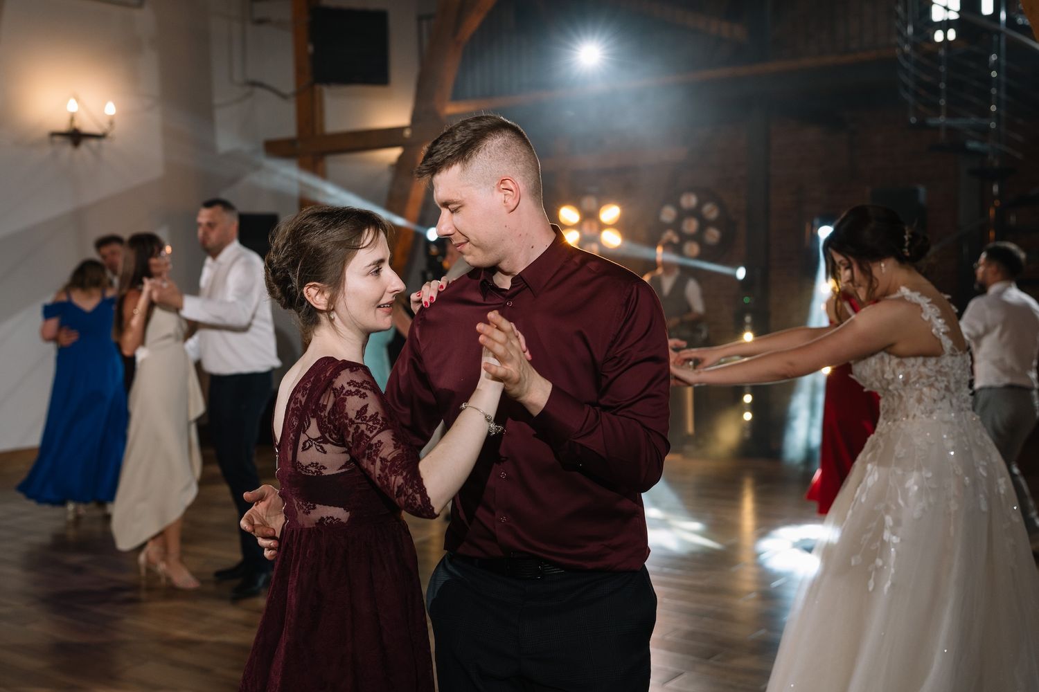 Young man in burgundy shirt dancing joyfully with a girl in a matching dress at a wedding reception.