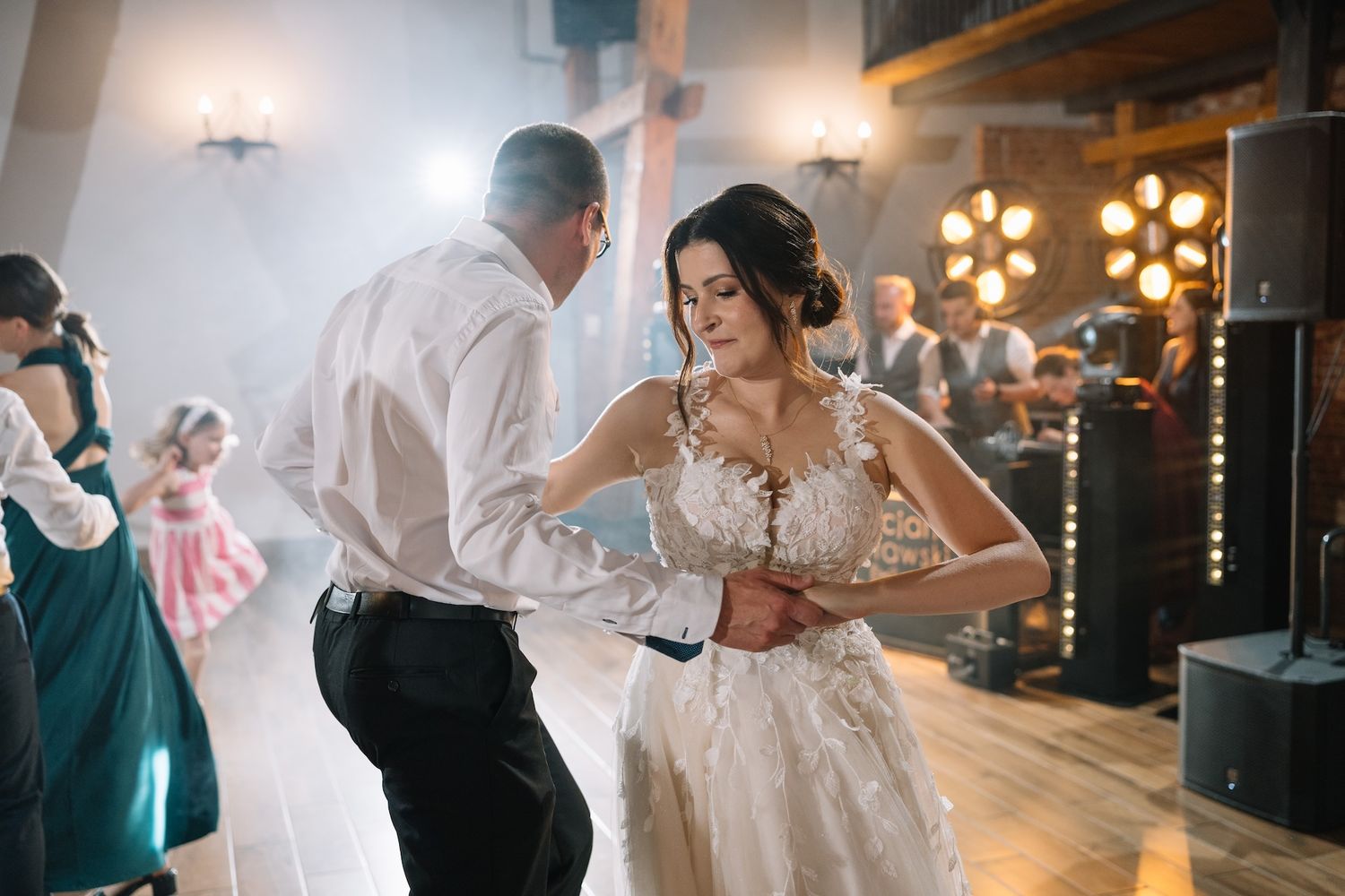 Bride in floral lace wedding gown dancing with partner on a misty dance floor at wedding reception.