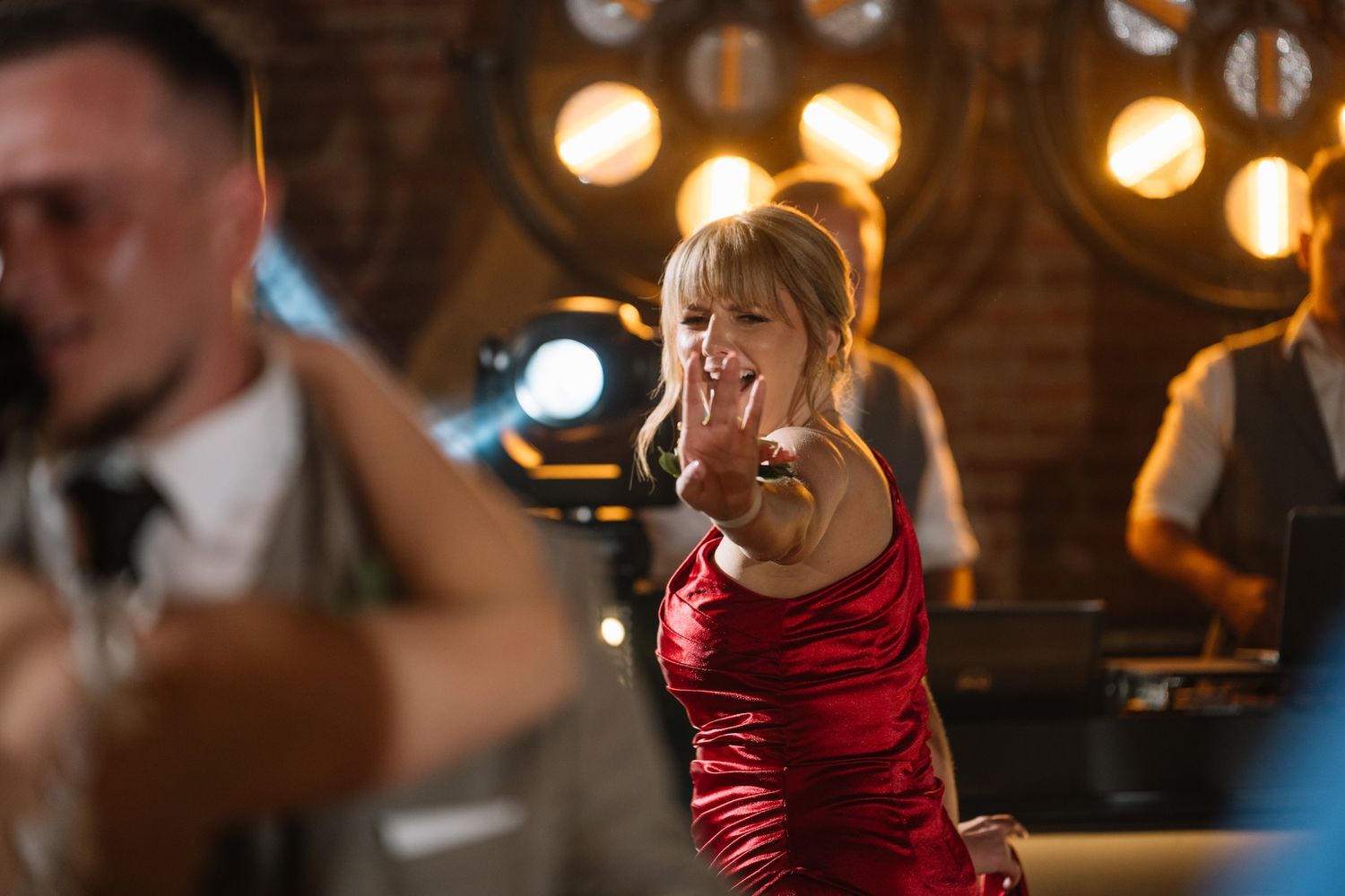 Woman in red dress dancing and reaching toward camera at a lively party event.