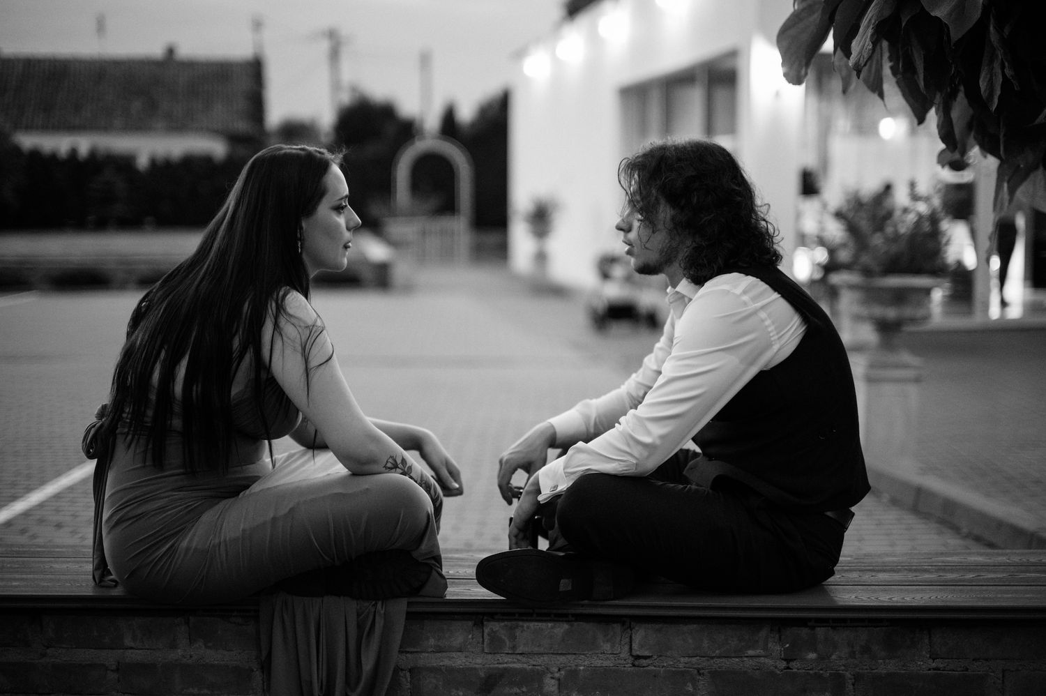 Black and white photo of two people sitting outdoors on steps in conversation.