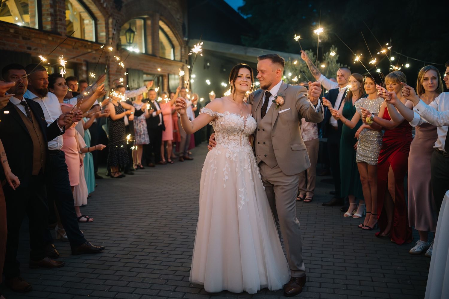 Bride and groom walking through sparkler send-off with wedding guests cheering.