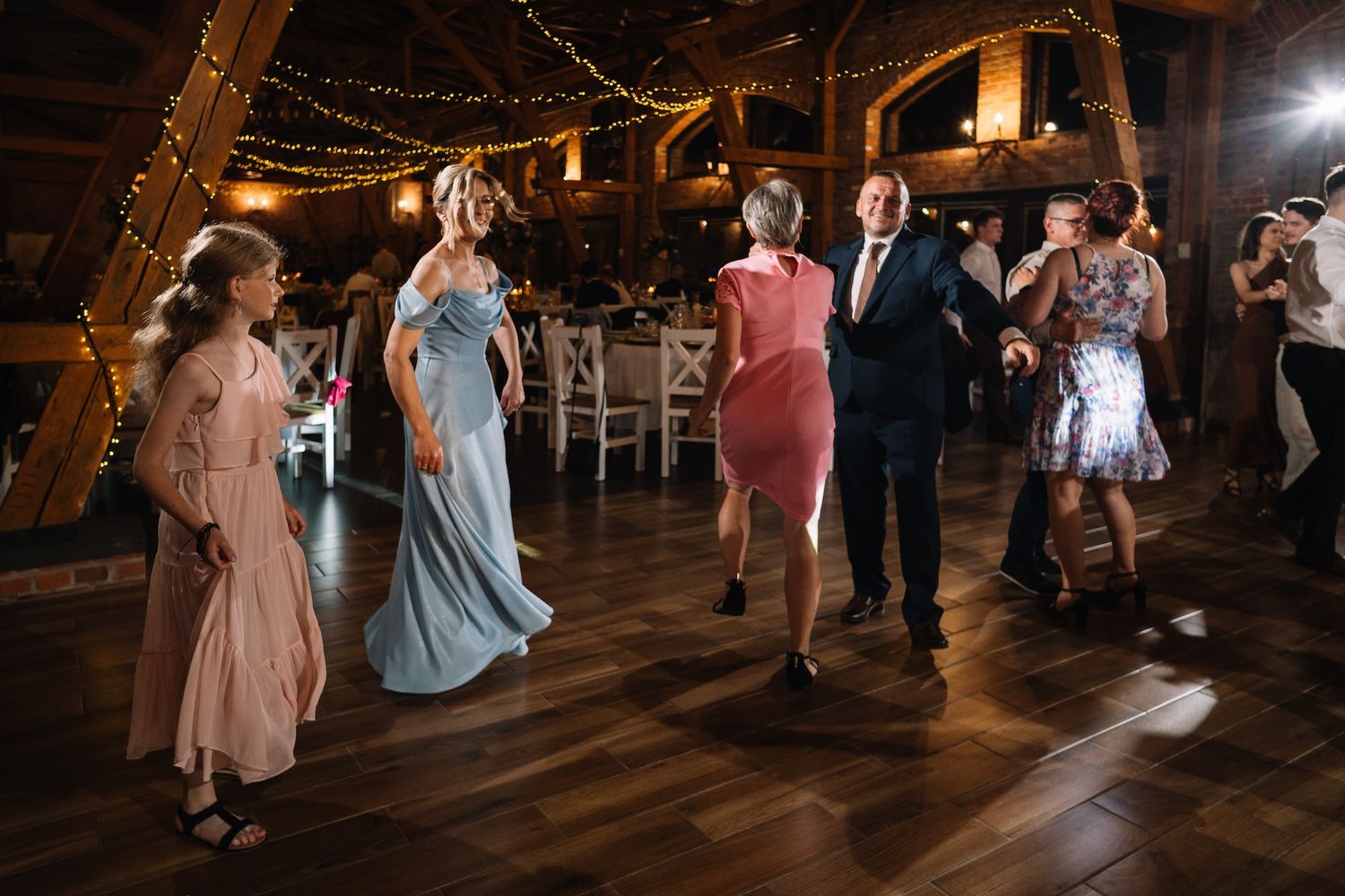 Wedding guests dancing together in elegant rustic barn venue with warm string lights.