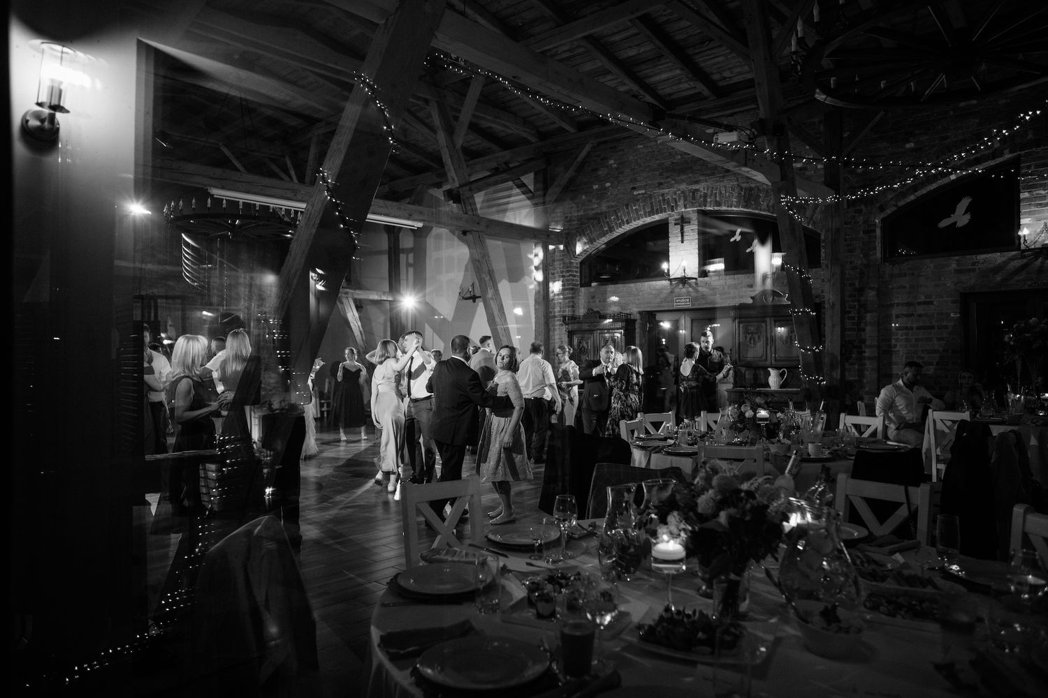 Black and white photo of elegant wedding reception guests mingling in a rustic barn venue.