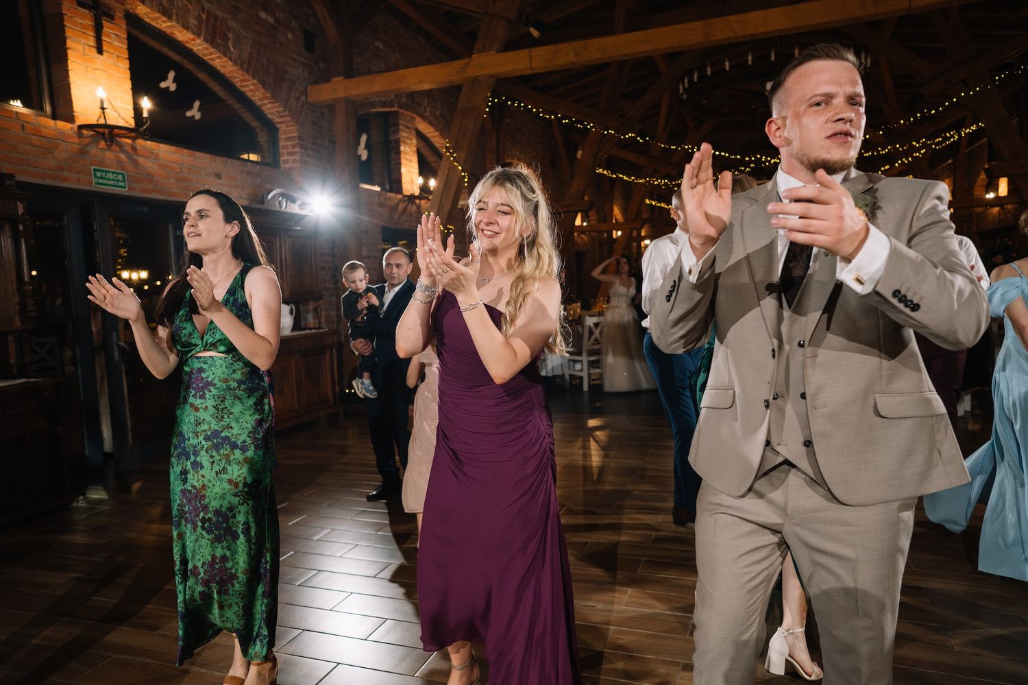 Wedding guests in formal attire clap and celebrate on a rustic barn reception dance floor.