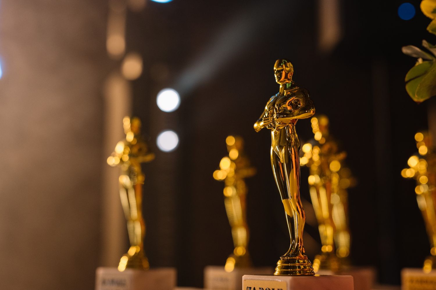 Row of golden Oscar-style award statuettes displayed on a stage with dramatic lighting.